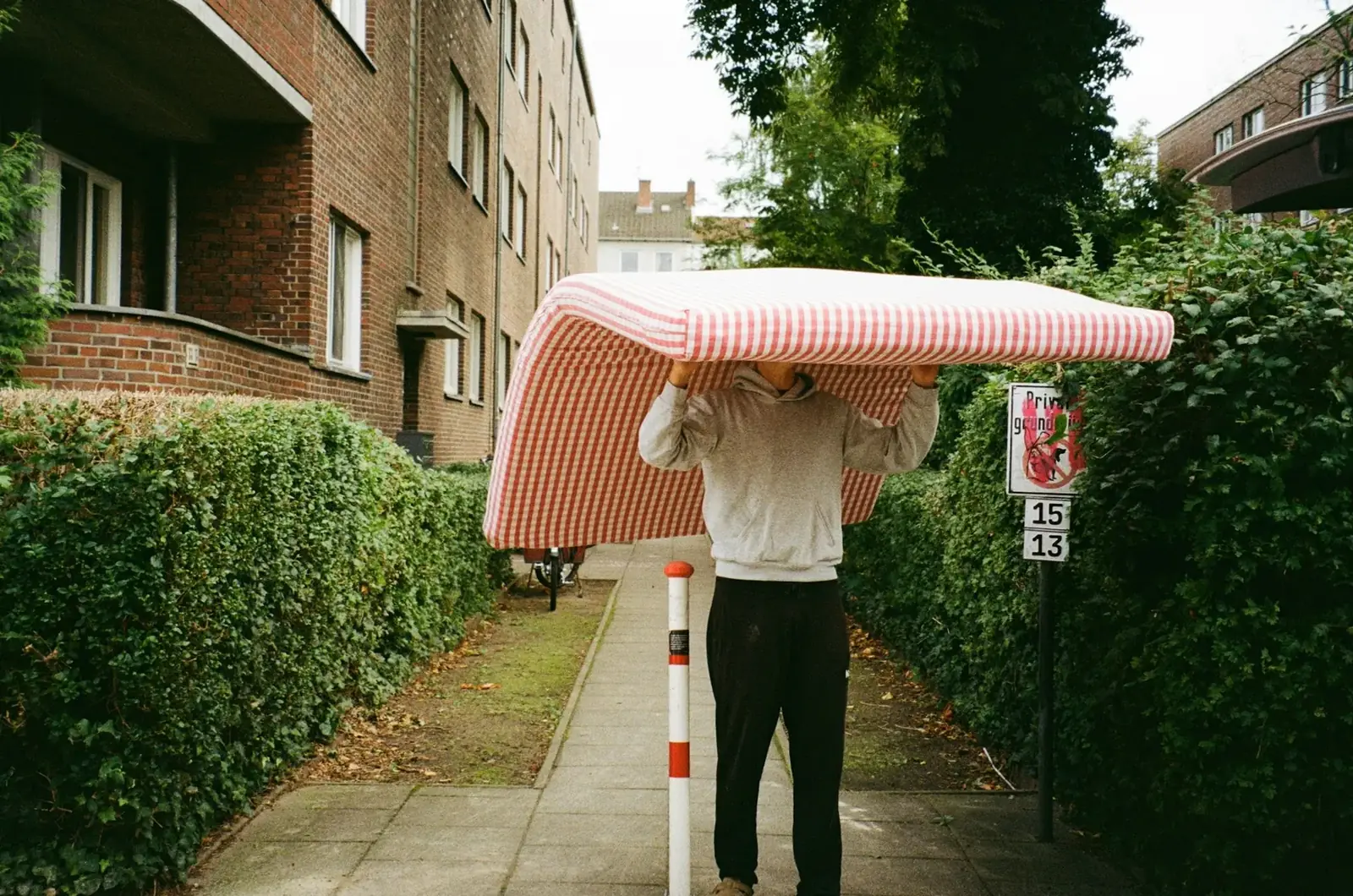 Man carrying a mattress over his head along a residential sidewalk