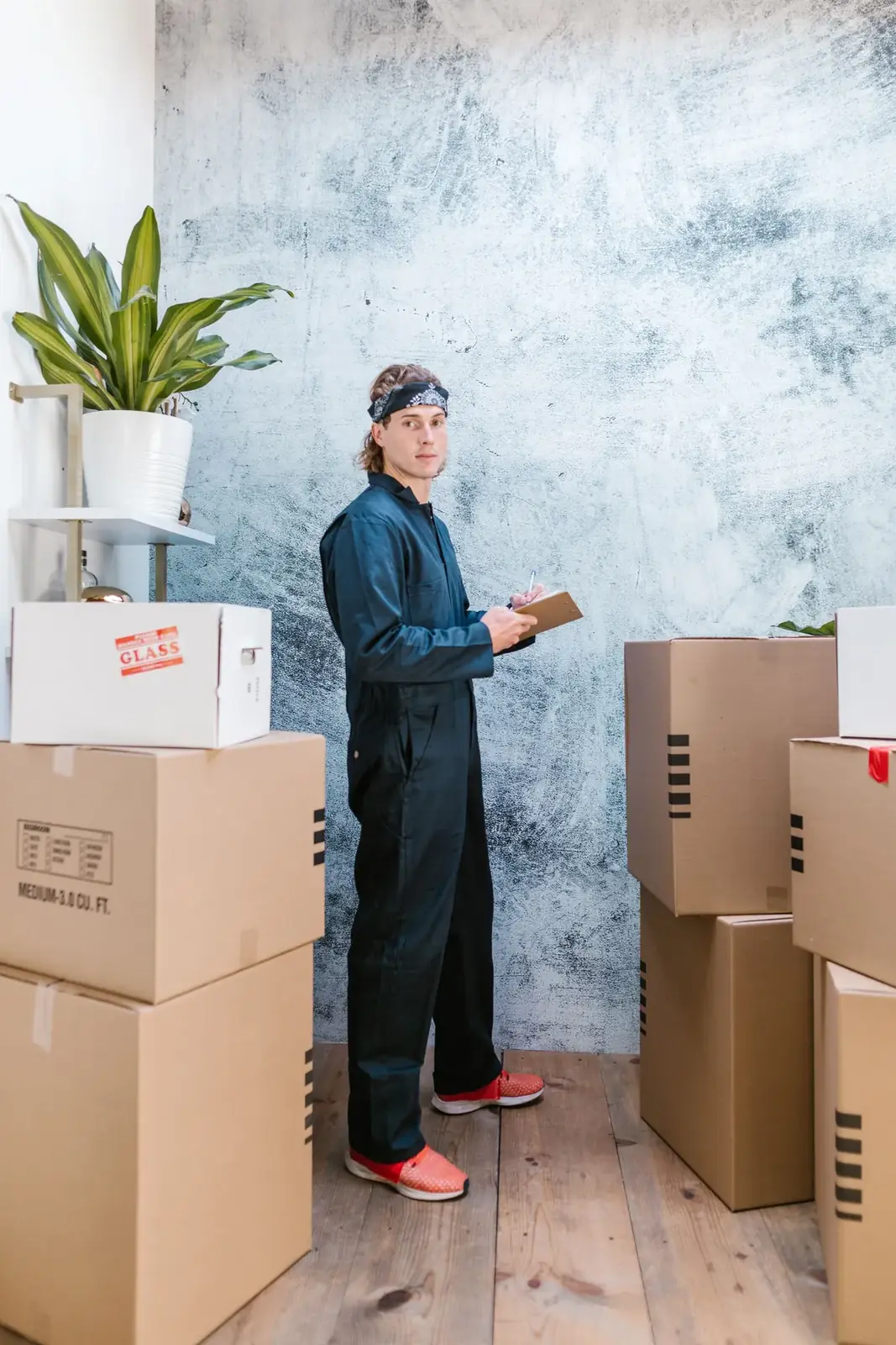 Mover in coveralls checking an inventory clipboard among stacked moving boxes